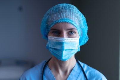Portrait of caucasian female doctor in hospital wearing face mask, medical cap and scrubs. medical professional at work during coronavirus covid 19 pandemic.